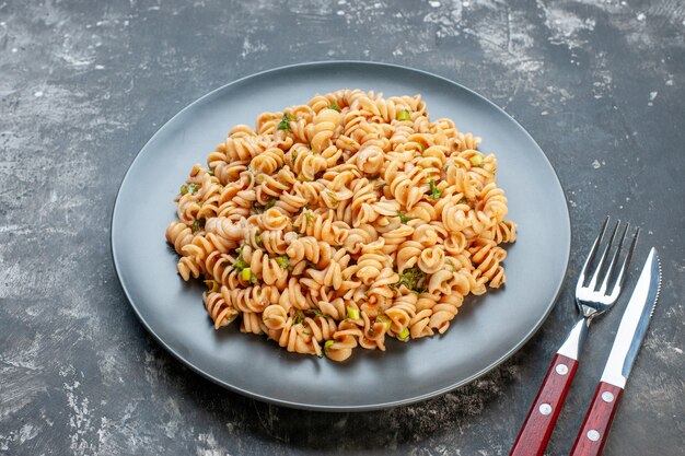 Bottom view rotini pasta on round plate fork and knife on dark table