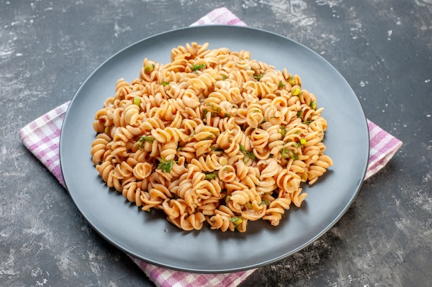 Bottom view rotini pasta on round plate on pink white checkered napkin on grey table