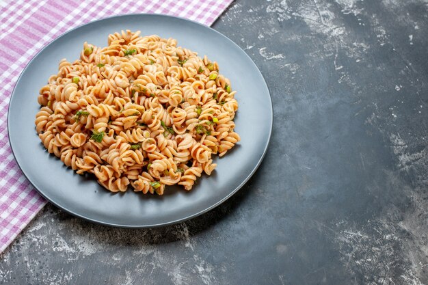 Bottom view rotini pasta on round plate on pink white checkered tablecloth on dark surface with free space