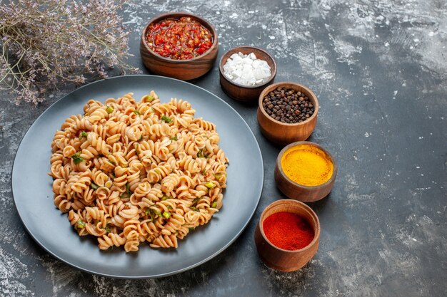 Free photo bottom view rotini pasta on round plate tomato sauce different spices in small bowls on dark table