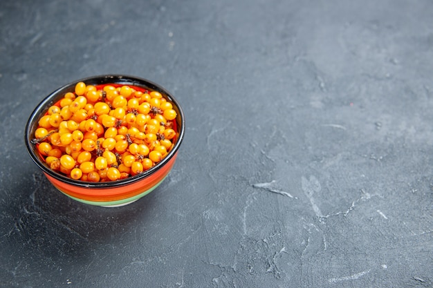 Bottom view sea buckthorn in bowl on dark red surface copy space