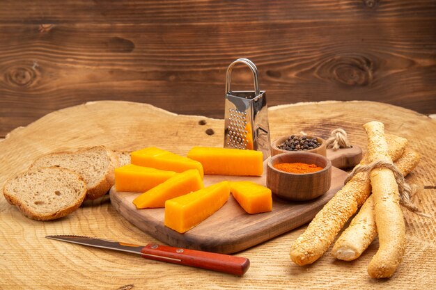 Вид снизу кусочки терки для сыра, разные специи в маленьких мисках на разделочной доске, нож, хлеб на деревянной земле