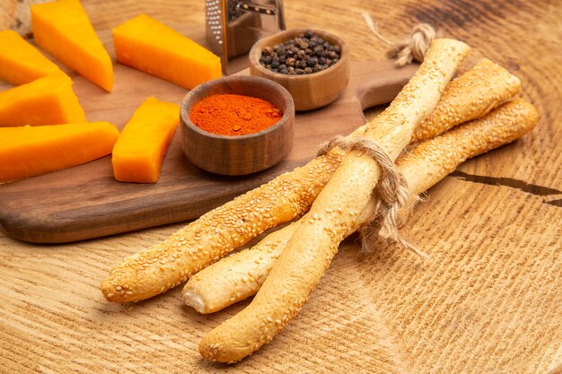 Bottom view slices of cheese box grater spices on cutting board knife bread slices on wooden ground