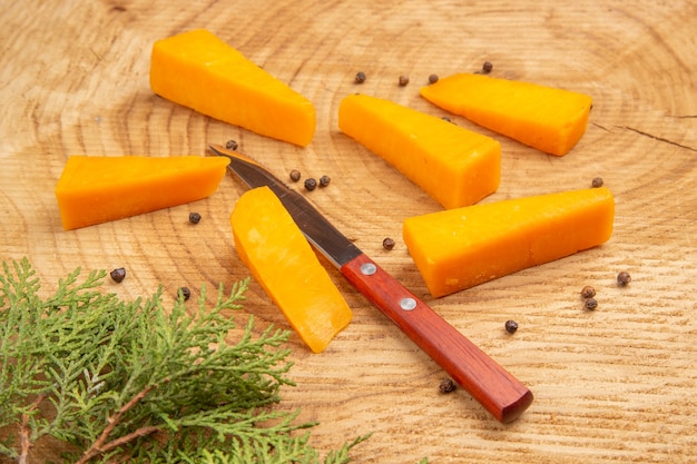 木製のテーブルにチーズが散らばった黒胡椒ナイフ松の木の枝の底面図スライス