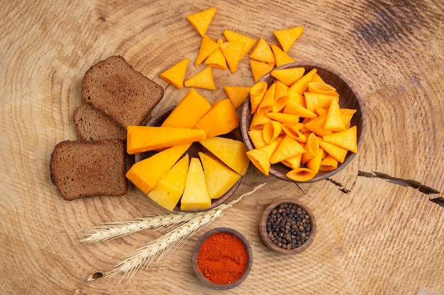 Foto gratuita fette di formaggio di trucioli di pane sparse da una ciotola di spighe di grano pepe nero e rosso sul tavolo di legno