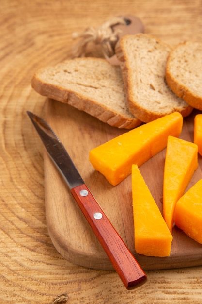 Bottom view slices of cheese slices of bread knife on chopping board on wooden surface