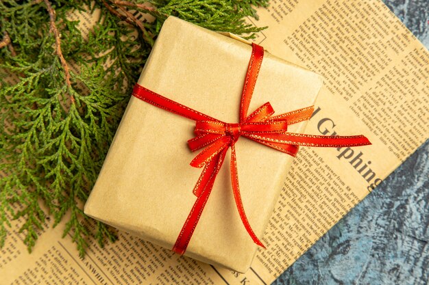 Bottom view small gift tied with red ribbon on newspaper on dark background