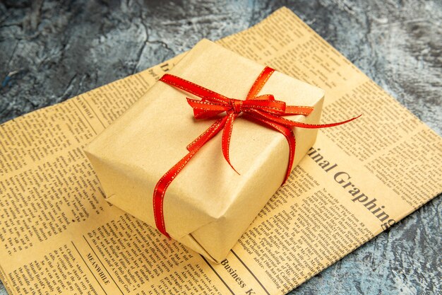 bottom view small gift tied with red ribbon on newspaper on dark