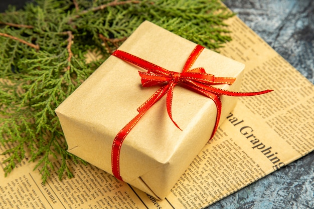 Bottom view small gift tied with red ribbon pine branch on newspaper on dark