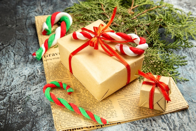 Вид снизу небольшой подарок, перевязанный красной лентой, рождественские конфеты на газете на сером фоне