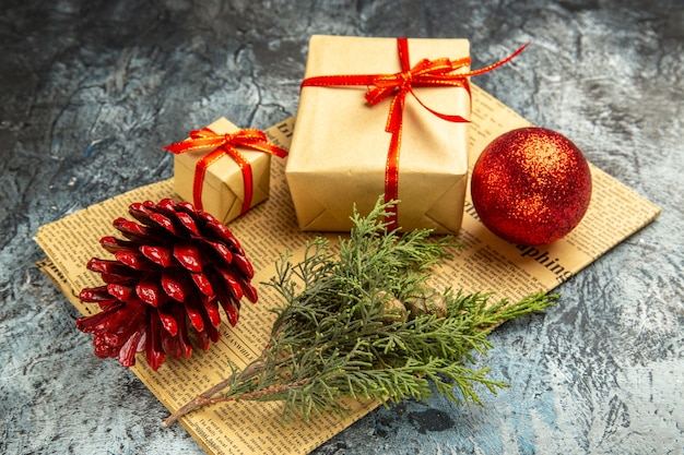 Bottom view small gifts tied with red ribbon red ball pine branch on newspaper on dark background