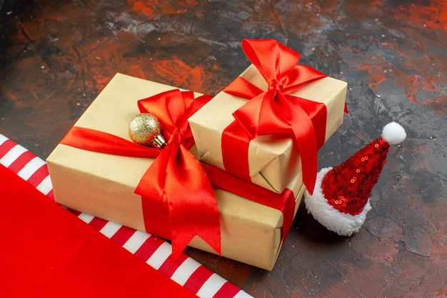 Bottom view small gifts tied with red ribbon santa hat on dark red table