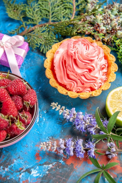 Вид снизу небольшой пирог с розовым кондитерским кремом, долькой лимона и ветвями малины на синем столе