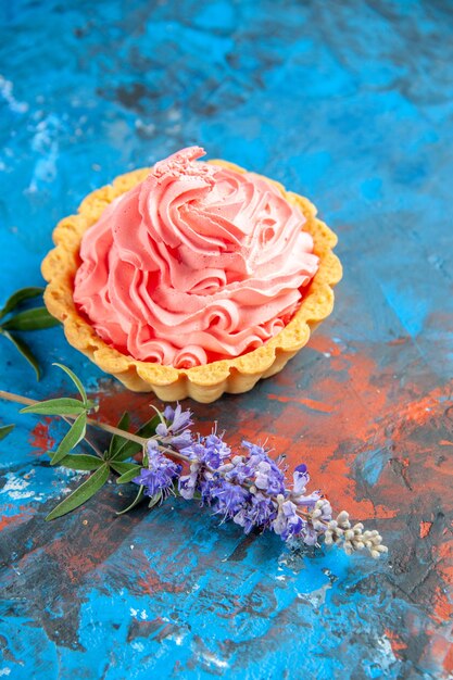 Bottom view small tart with pink pastry cream purple flowers on blue table