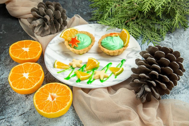 Vista dal basso piccole crostate con crema pasticcera verde e fetta di limone su piatto su scialle beige, pigne di arance tagliate su superficie scura