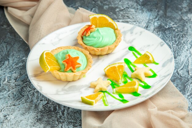 Bottom view small tarts with green pastry cream and lemon slice on plate beige shawl on dark surface