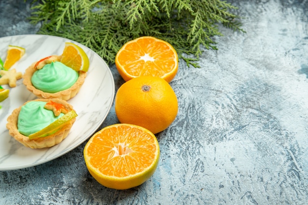 Bottom view small tarts with green pastry cream and lemon slice on plate cut oranges on dark surface free space
