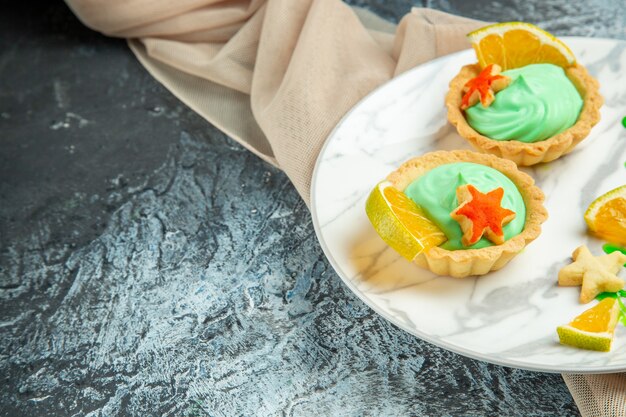 Bottom view small tarts with green pastry cream and lemon slice on plate on dark surface copy place