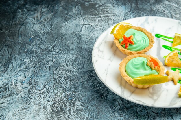 Bottom view small tarts with green pastry cream and lemon slice on plate on dark surface free space