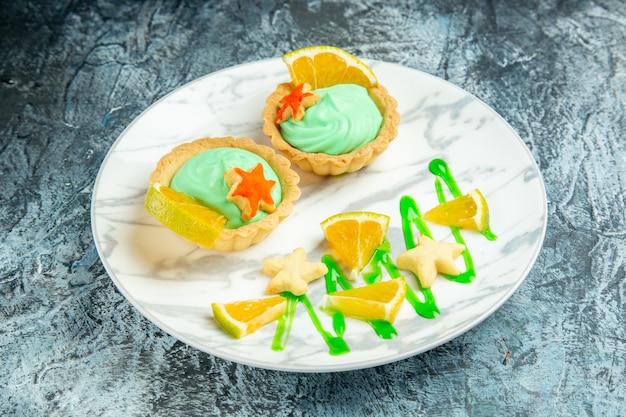 Bottom view small tarts with green pastry cream and lemon slice on plate on dark surface