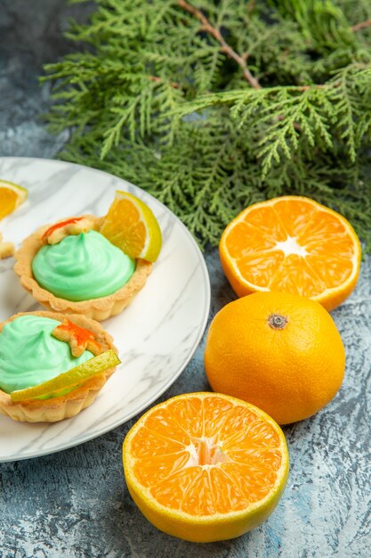 Bottom view small tarts with green pastry cream and lemon slices on plate cut oranges on dark surface