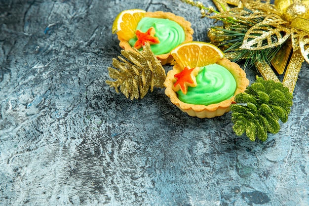 Вид снизу маленькие пирожные с рождественскими украшениями из зеленого кондитерского крема на серой поверхности с копией пространства