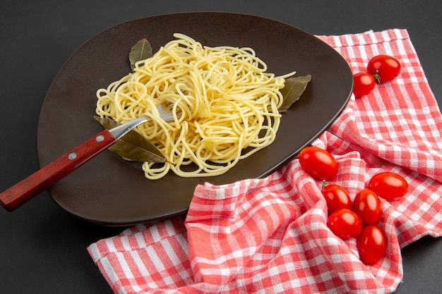 Bottom view spaghetti pasta with bay leaves fork on plate cherry tomatoes red and white checkered kitchen towel on black table