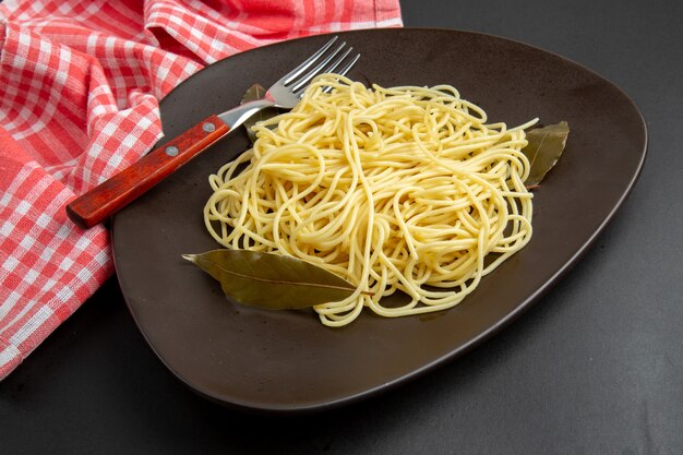 Вид снизу макароны спагетти с вилкой лаврового листа на скатерти на черном фоне