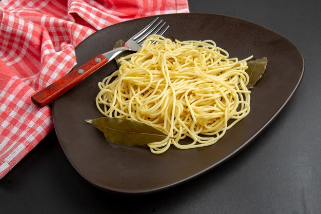 Bottom view spaghetti pasta with bay leaves fork on plate tablecloth on black background