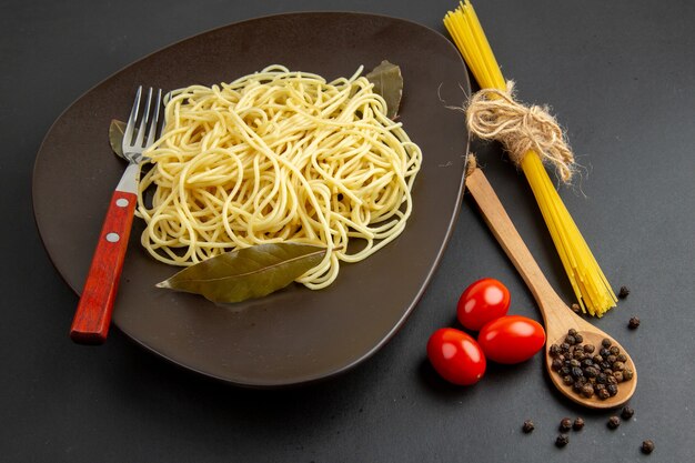 Вид снизу макароны спагетти с лавровыми листьями на тарелке, вилке деревянной ложкой помидоры черри на темном фоне