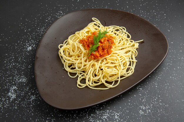 Вид снизу спагетти с вилкой для соуса на черной тарелке на черном столе