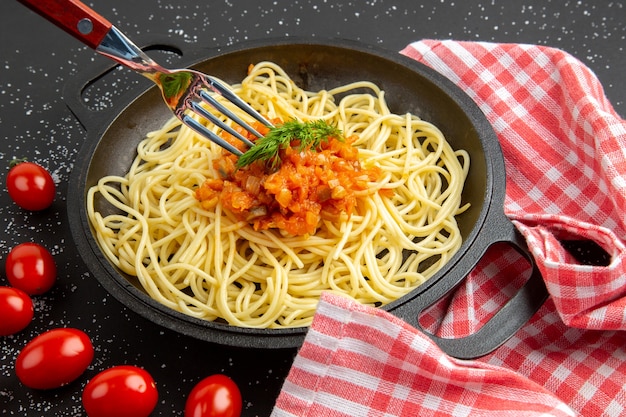 Спагетти с соусом на сковороде, вилка, помидоры черри на черном столе, вид снизу