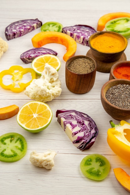 Bottom view spices bowls cauliflower cut bell pepper cut pumpkin cut red cabbage cut green tomatoes on white table