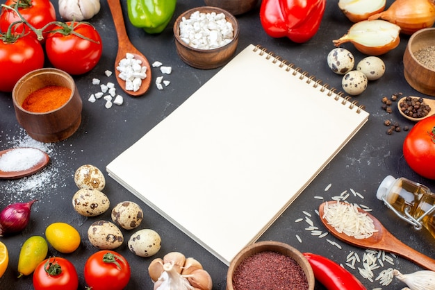 Bottom view spiral notebook rice sea salt in wooden spoons tomatoes quail eggs cumcuats peppers on black table