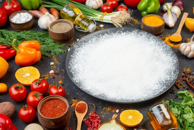 Bottom view sprinkled flour on round plate black pepper in small bowl tomatoes oil bottle coriander dill on table