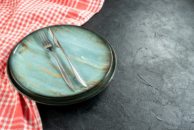 Forchetta in acciaio vista dal basso e coltello da cena sulla tovaglia a quadretti bianca e rossa del piatto rotondo sullo spazio libero della tavola nera
