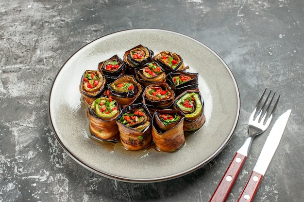 Bottom view stuffed eggplant rolls on white oval plate fork and knife on grey