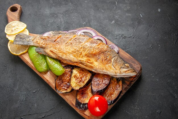 Bottom view tasty fish fry fried eggplants onion on wood serving board on dark background
