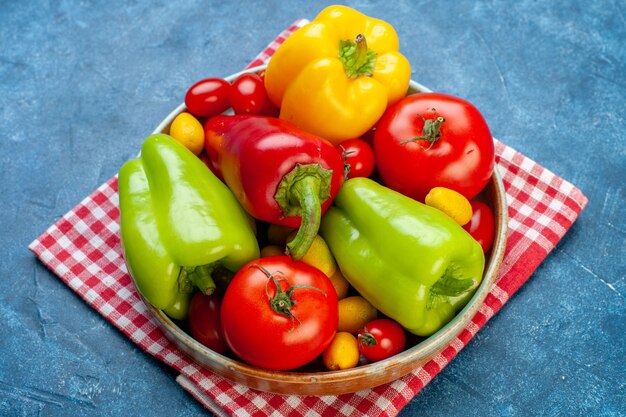 Free photo bottom view various vegetables cherry tomatoes different colors bell peppers tomatoes cumcuat on platter on red white checkered kitchen towel on blue table