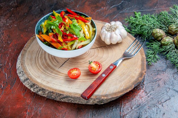 Bottom view vegetable salad in bowl fork garlic on rustic board fir branch on dark red table