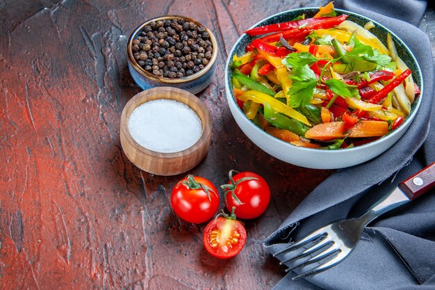 Bottom view vegetable salad in bowl ultramarine blue shawl cherry tomatoes spices fork on dark red table