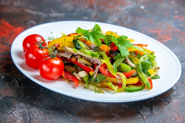 Free photo bottom view vegetable salad cherry tomatoes on oval plate on dark red isolated surface