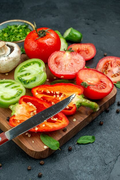 Bottom view vegetables green and red tomatoes bell peppers knife on cutting board greens in bowl on black table