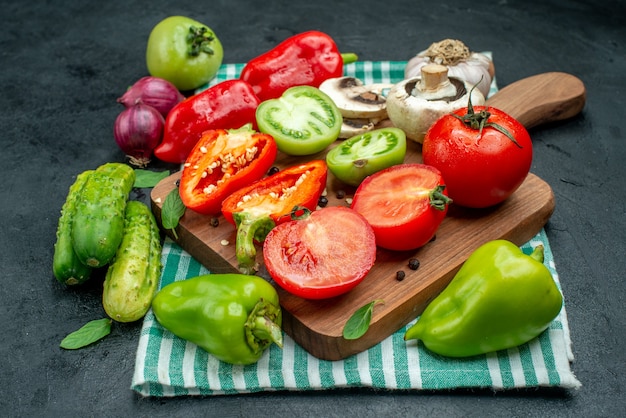 Bottom view vegetables mushrooms tomatoes bell peppers on cutting board garlic cucumbers red onion on black table