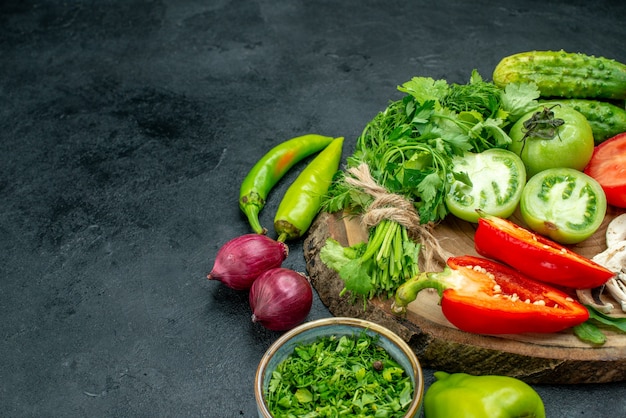 Free photo bottom view vegetables tomatoes bell peppers cucumbers greens on wood board bowl with greens onions on black table free space