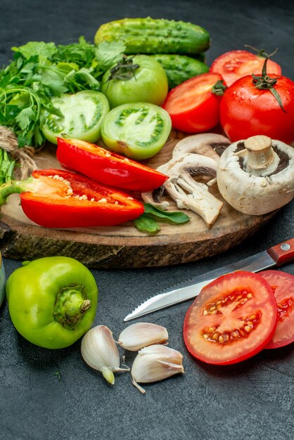 Bottom view vegetables tomatoes bell peppers cucumbers greens on wood board knife on black table