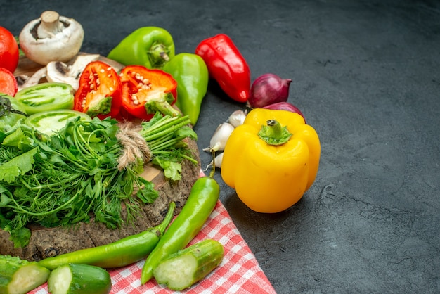 Bottom view vegetables tomatoes red bell peppers greens on rustic board hot peppers on tablecloth on black table