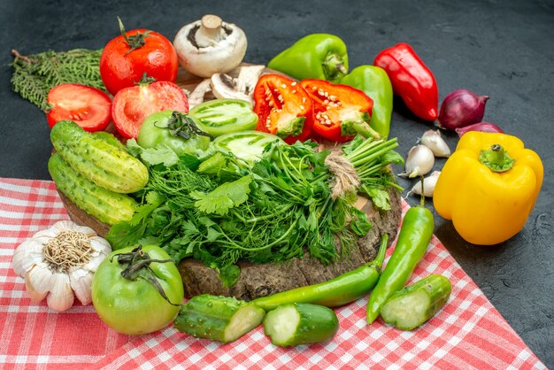 Bottom view vegetables tomatoes red bell peppers greens on wood board hot peppers garlic on tablecloth on black table