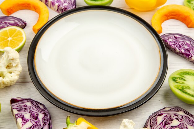 Bottom view white round platter cut vegetables on white wooden table