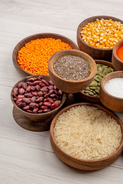 Bottom view wooden bowls with beans rice black pepper pumpkin seeds turmeric salt lentiles on grey table